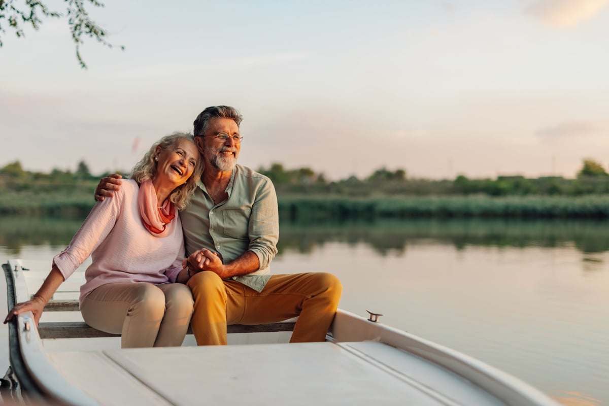 Pareja de jubilados felices riendo durante un paseo en barco a la puesta de sol